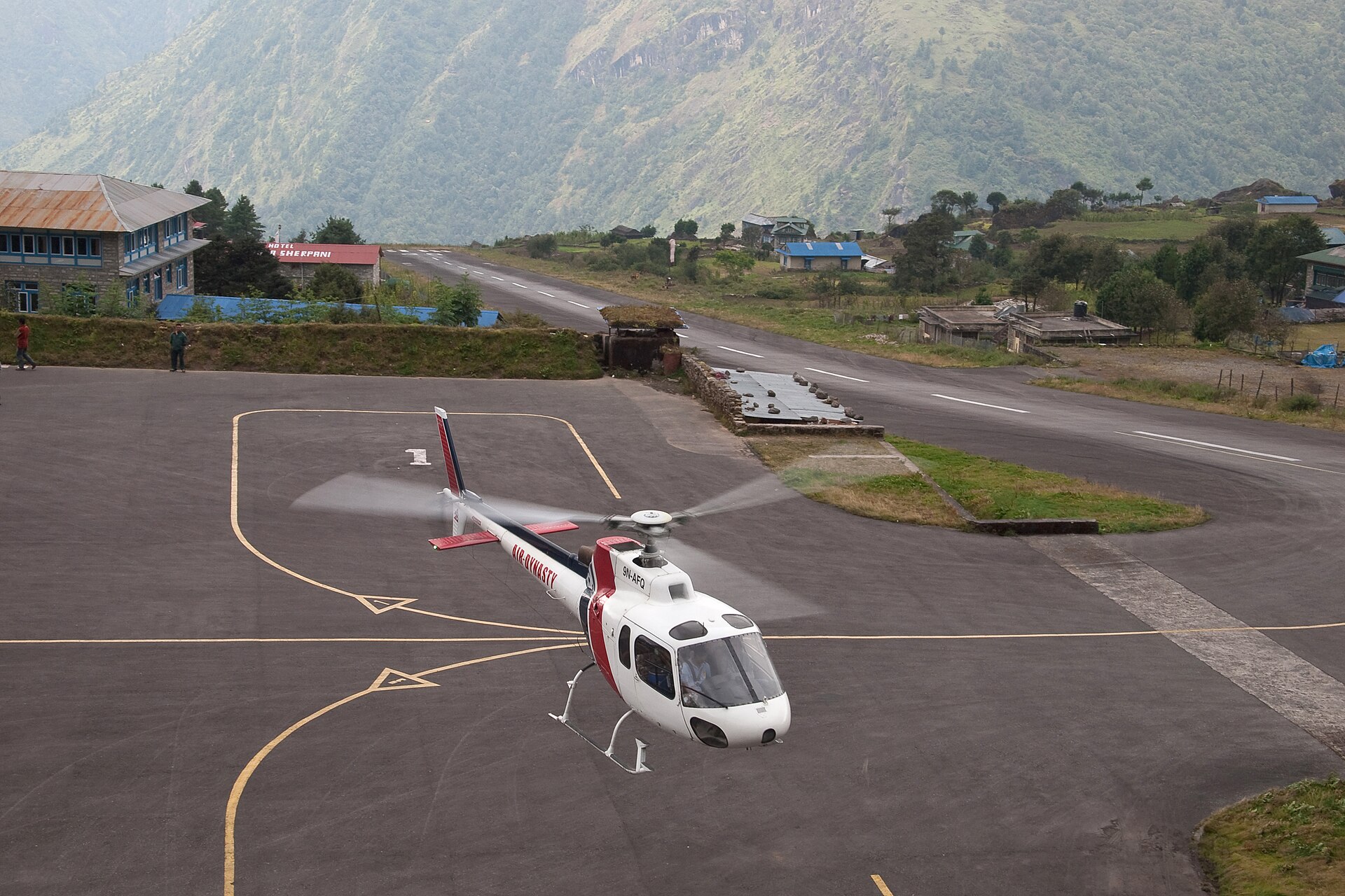 An AS350 running up on the Lukla apron, the airstrip climbing away behind it.